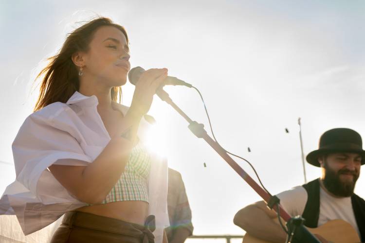 Girl standing behind a microphone while a man sits beside her with a guitar