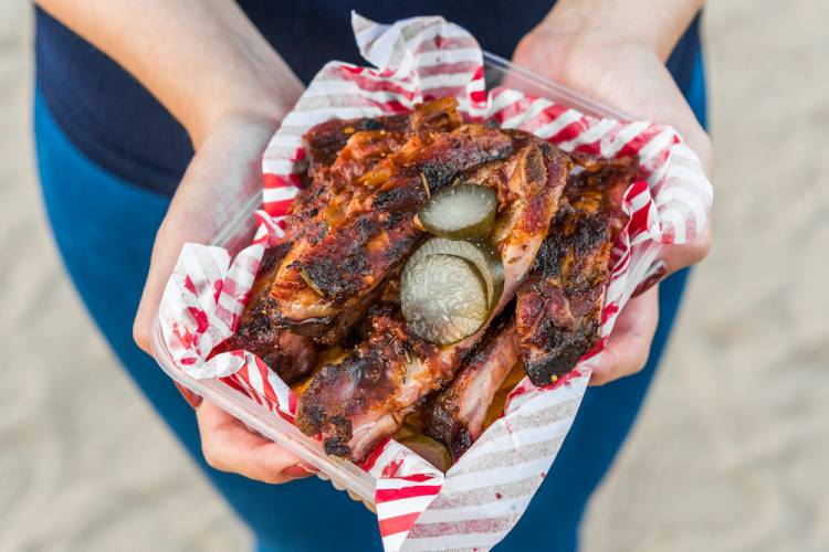 person with street festival food in hand, barbecue food with red and white checkered wax paper and paper plate
