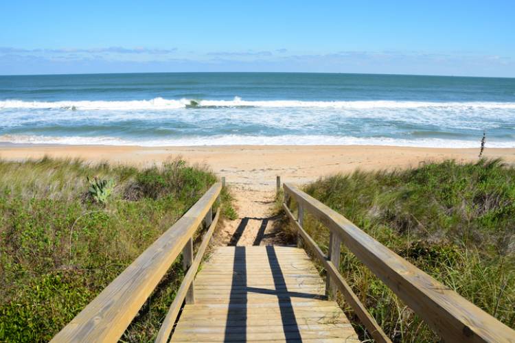 boardwalk to st augustine beach in florida with waves crashing on the shore and bright blue skies