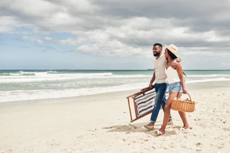 young couple walking along the beach with chairs and picnic items in hand