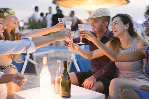 young group of people in neutral clothing cheers wine glasses on a beach young group of people in neutral clothing cheers wine glasses on a beach