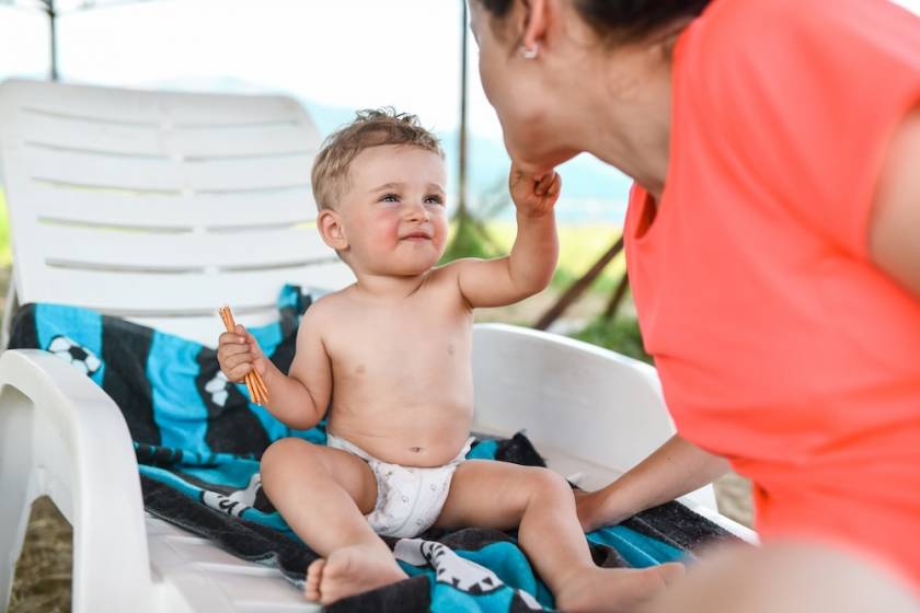 baby on beach chair eating snacks and interacting with mother