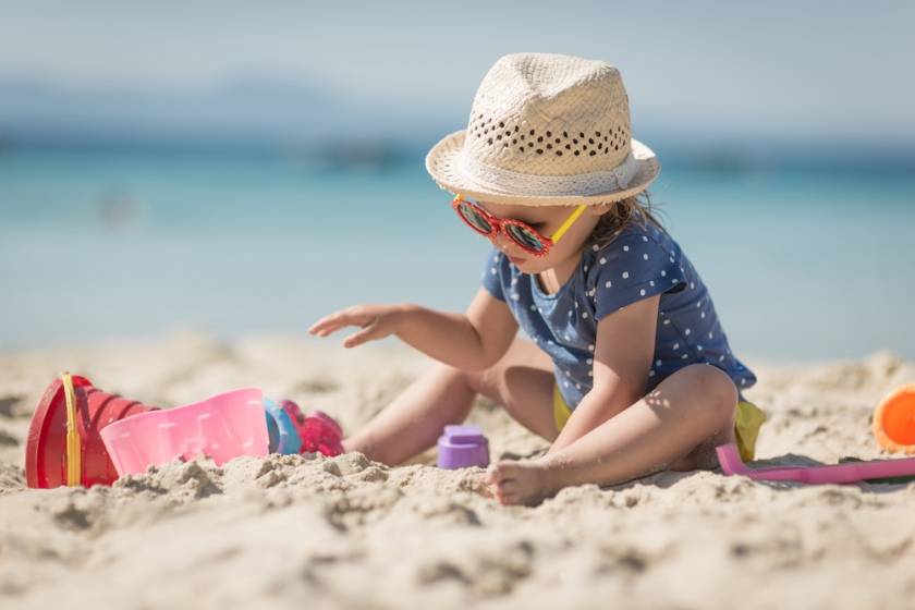 baby wearing hat and sunglasses playing in sand on beach